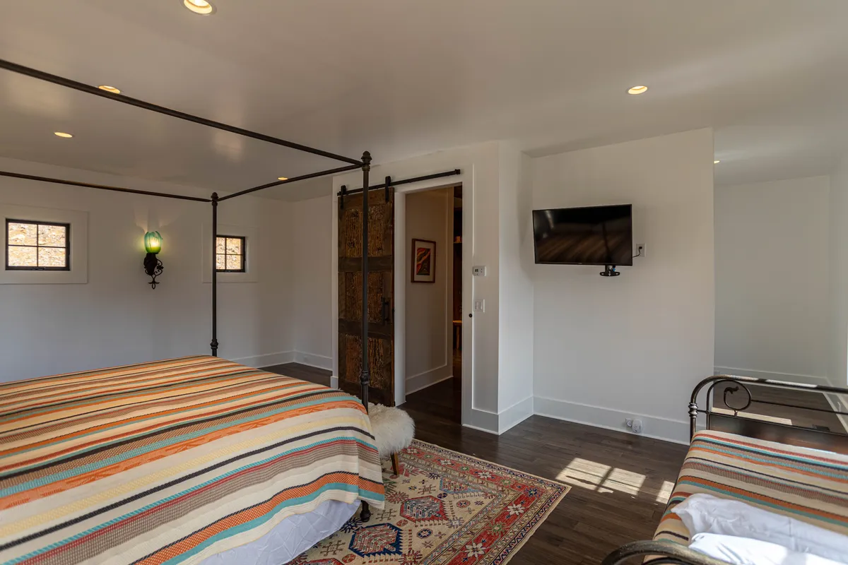 A bedroom with twin canopy beds dressed in colorful, striped bedding, a rug, and a wall-mounted TV. The space feels playful yet cozy, with options for both relaxation and entertainment for guests of all ages.