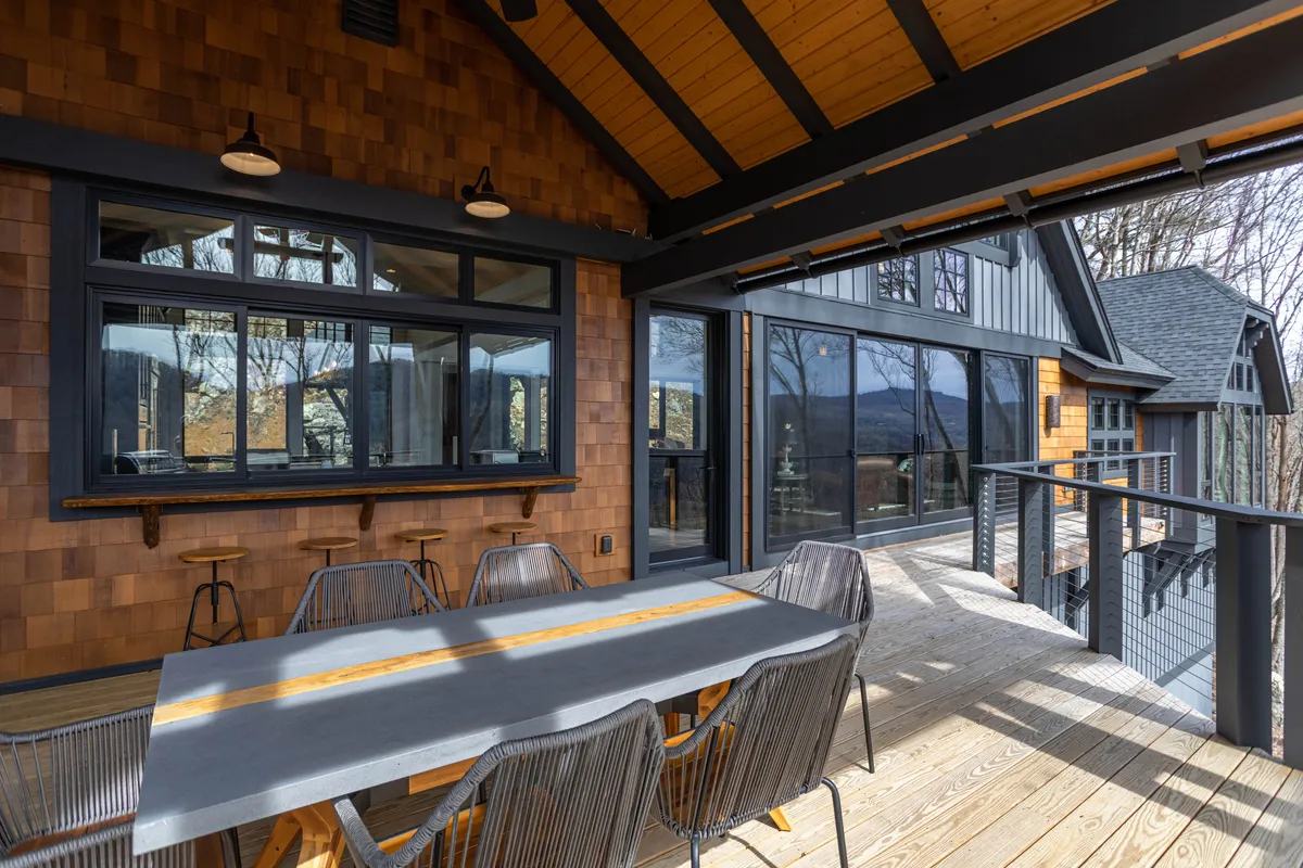 A large outdoor dining table set amidst nature, with panoramic windows nearby. The serene setting is ideal for group dining, relaxation, and soaking in the surrounding landscape during any season, day or night.