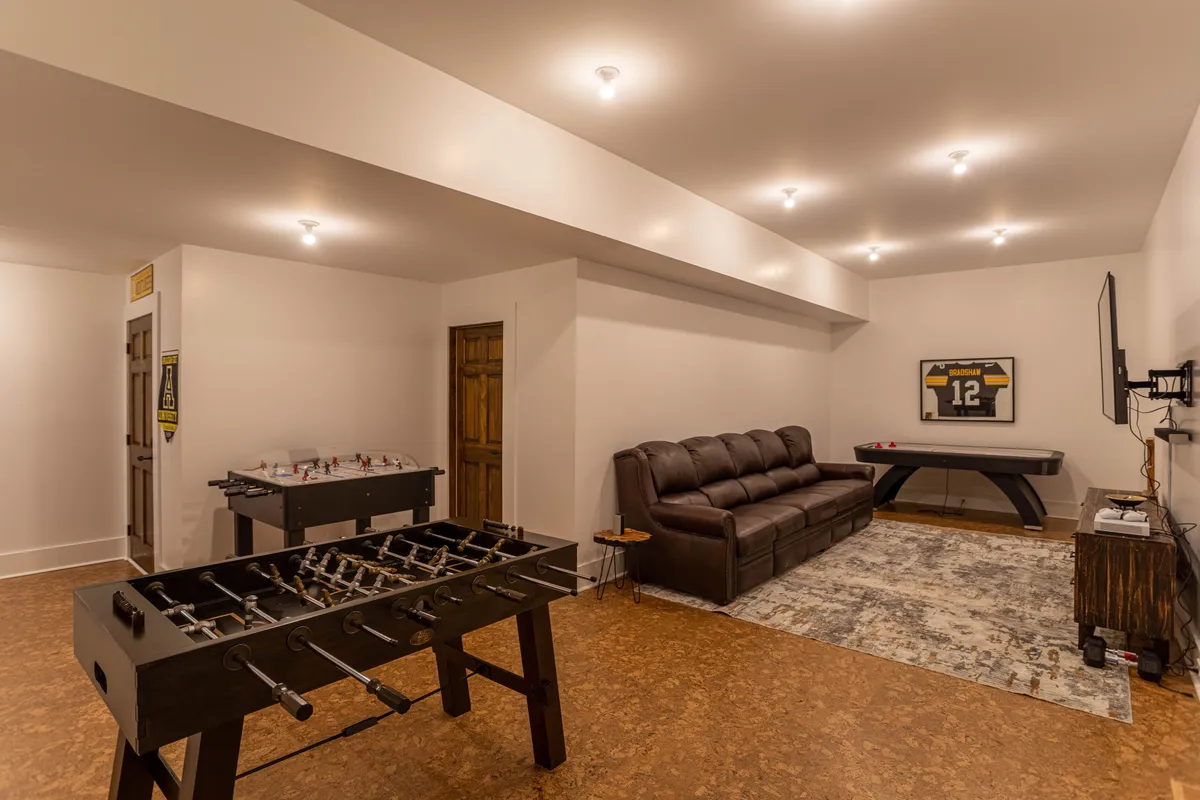 A cozy interior with a foosball table, leather sofa, plush rug, television, and decorative wall art. The spatial arrangement encourages both gaming and lounging, ideal for family or group game nights and watching sports or movies together.