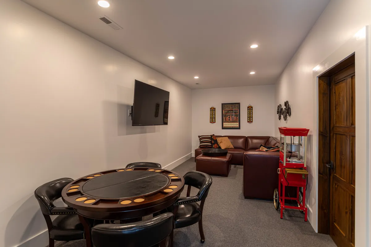 This image features an entertainment lounge with a poker table, leather sofa, television, popcorn machine, and decorative wall art. The space is designed for relaxation and various forms of entertainment, embodying the ultimate game and movie zone vibe.