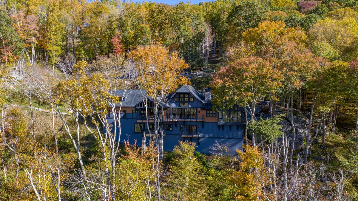 This exterior image captures the house nestled among tall trees with colorful foliage, creating a backdrop that highlights the beauty of seasonal changes. The surrounding landscape suggests opportunities for hiking, nature walks, and outdoor gatherings, echoing the section's emphasis on seasonal activities.
