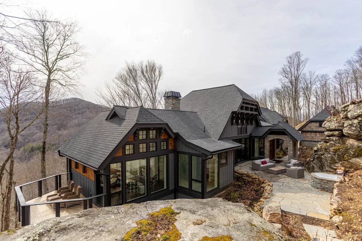 This image showcases the modern architecture of Bouldercrest, surrounded by a natural mountain landscape. The outdoor seating area offers a welcoming space for guests to relax while taking in panoramic views. The patio and fire pit provide a perfect spot for tranquil evenings or social gatherings under the stars.