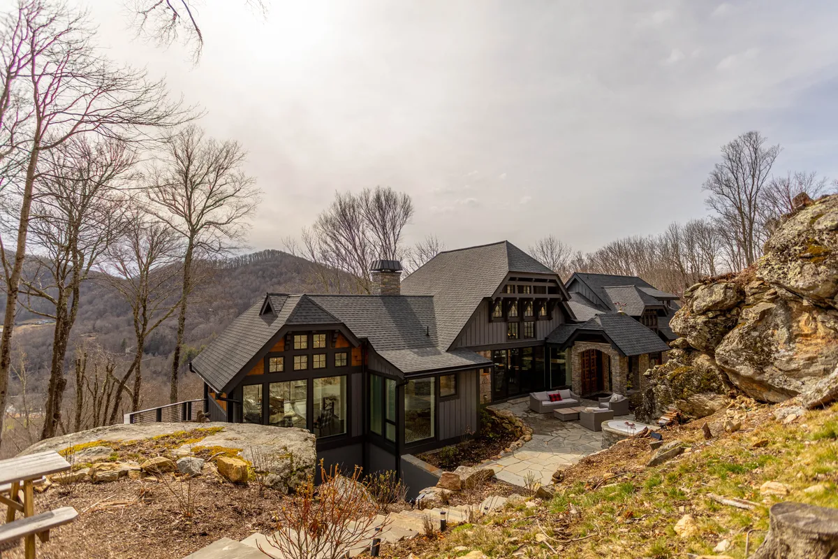This photo presents the house framed by its dramatic mountain surroundings, an inviting outdoor seating area, and a relaxed patio ambiance. The natural rock formations and garden space suggest opportunities for both relaxation and play for all ages.