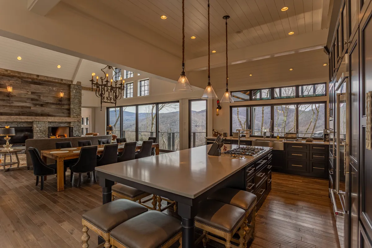 An open-concept space seamlessly integrating a large custom dining table and a modern, fully-equipped kitchen. The dining area is ideal for family feasts or intimate meals, and large windows offer scenic views. The kitchen features a central island and modern appliances, visually connecting the culinary space to the communal areas.
