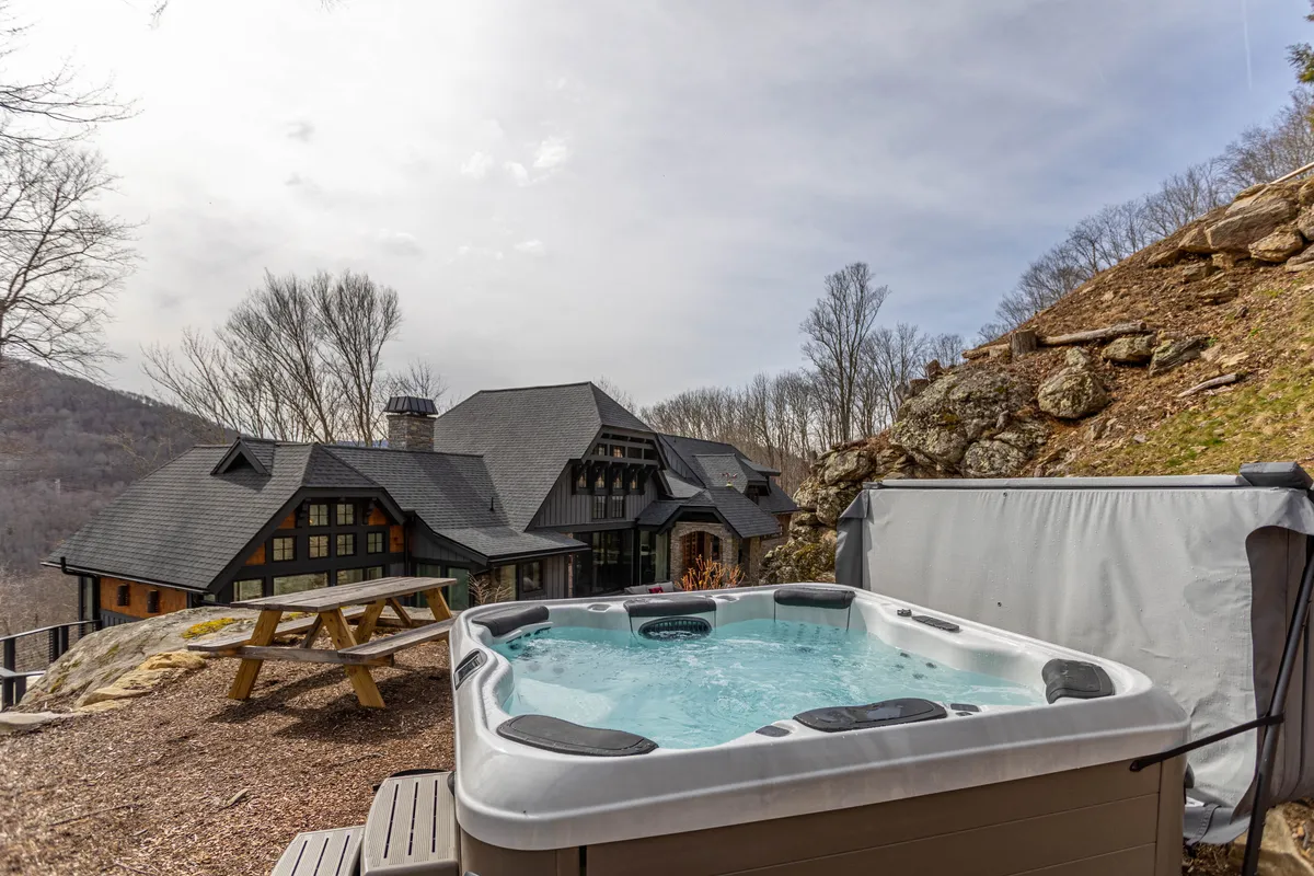 This image features a private hot tub and picnic table set against a breathtaking mountain view. The surrounding natural landscape and open sky suggest both daytime and nighttime enjoyment, immersing guests in a tranquil, rejuvenating outdoor experience.